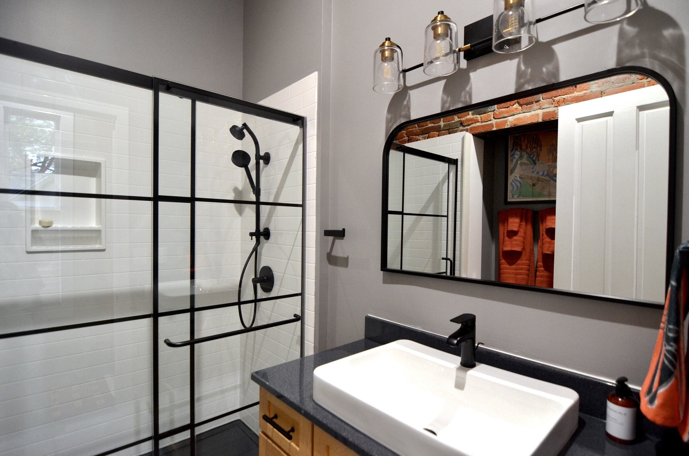 Completed bathroom remodel with a black framed shower and brick feature wall